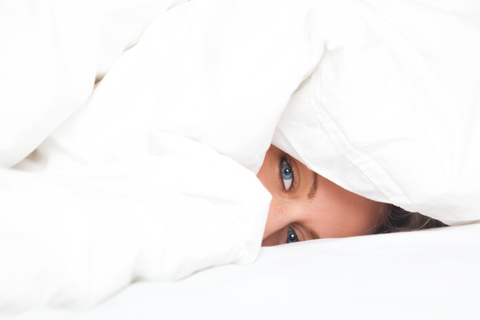 young woman in bed under blanket, suffering from a migraine headache