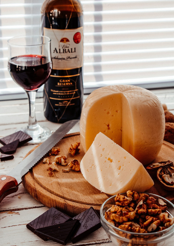 bottle and glass of red wine on a table top with cheese, nuts, and chocolate, some potential migraine triggers