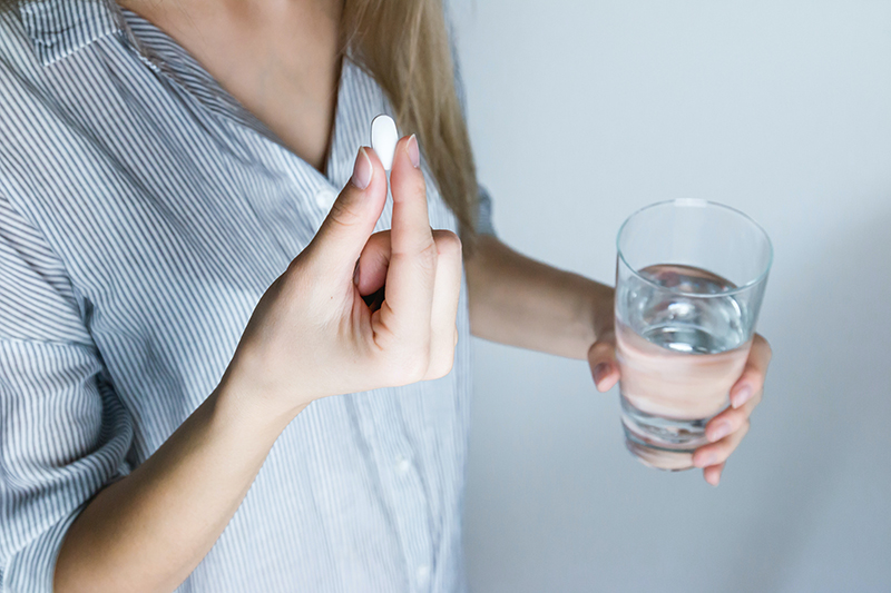 A woman taking a pill for a migraine headache, holding a glass of water